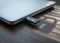 Clé de sécurité matérielle branchée sur un ordinateur portable fermé, ombre de cadenas sur un bureau en bois