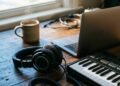 Casque de studio, clavier MIDI et ordinateur portable sur un bureau en bois, à la lumière du matin