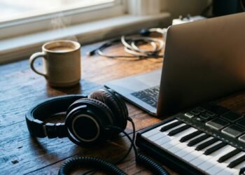 Casque de studio, clavier MIDI et ordinateur portable sur un bureau en bois, à la lumière du matin