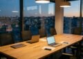 Salle de réunion vide au crépuscule, ordinateurs portables ouverts sur la table face aux toits de la ville