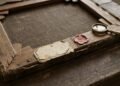 Dos d’une toile ancienne sur une table en bois : châssis, étiquette jaunie, cachet de cire rouge et loupe en laiton