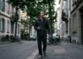 Homme qui marche dans une rue arborée en parlant à voix haute, écouteurs sans fil et téléphone en main