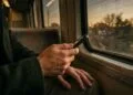 Mains d’un voyageur qui tient son smartphone dans un train, au coucher du soleil